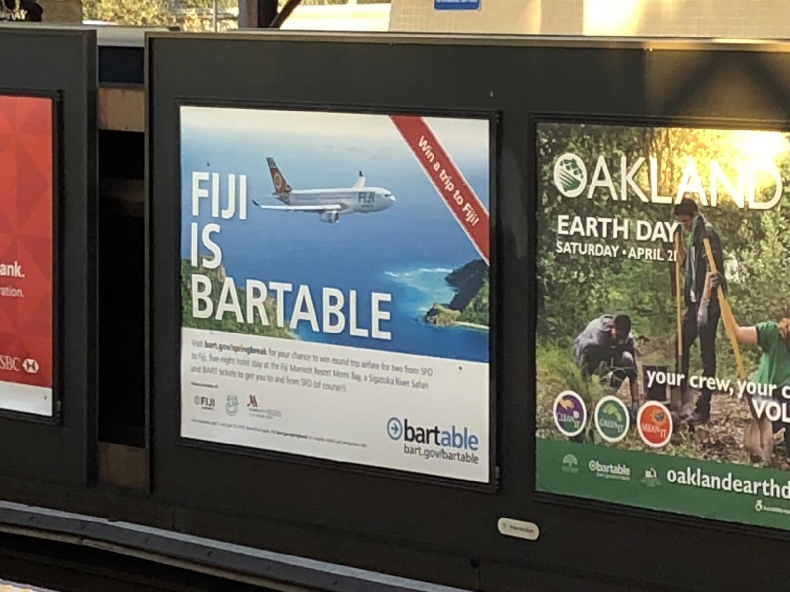 A BARTable destination campaign displayed alongside other posters on a BART platform.